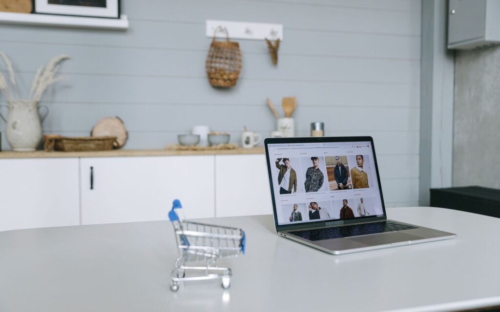 Laptop displaying an online shop beside a miniature shopping trolley