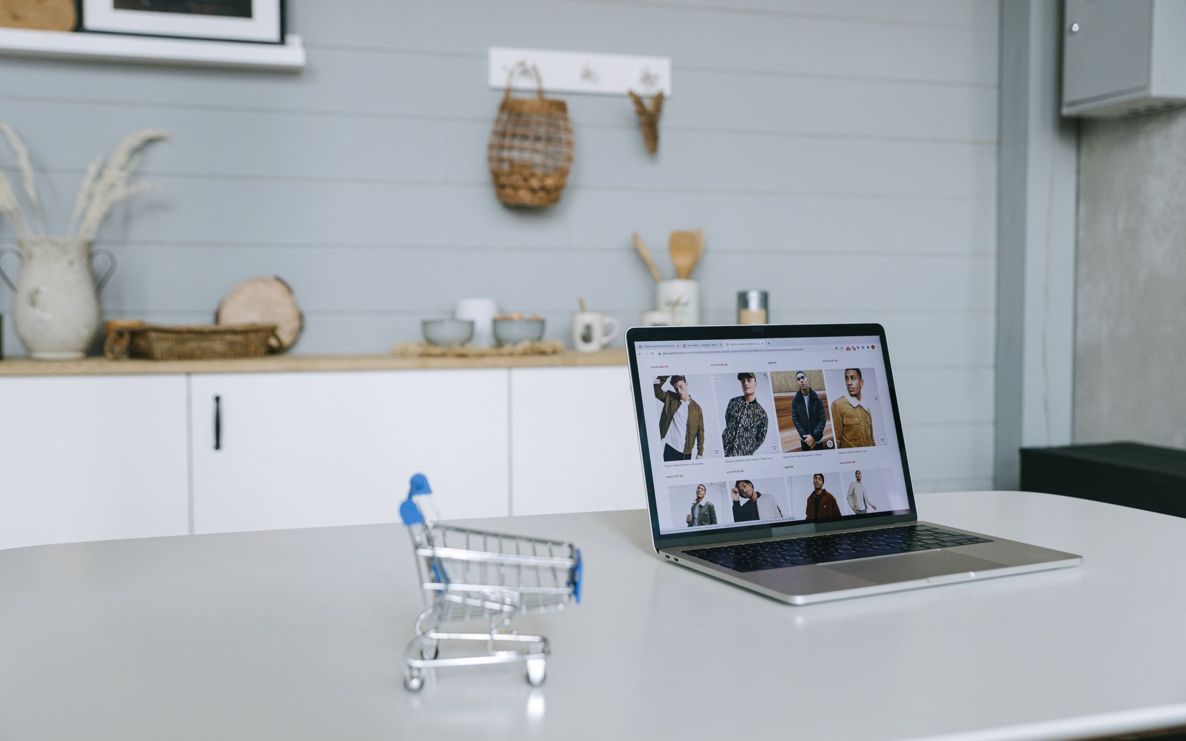 Laptop displaying an online shop beside a miniature shopping trolley