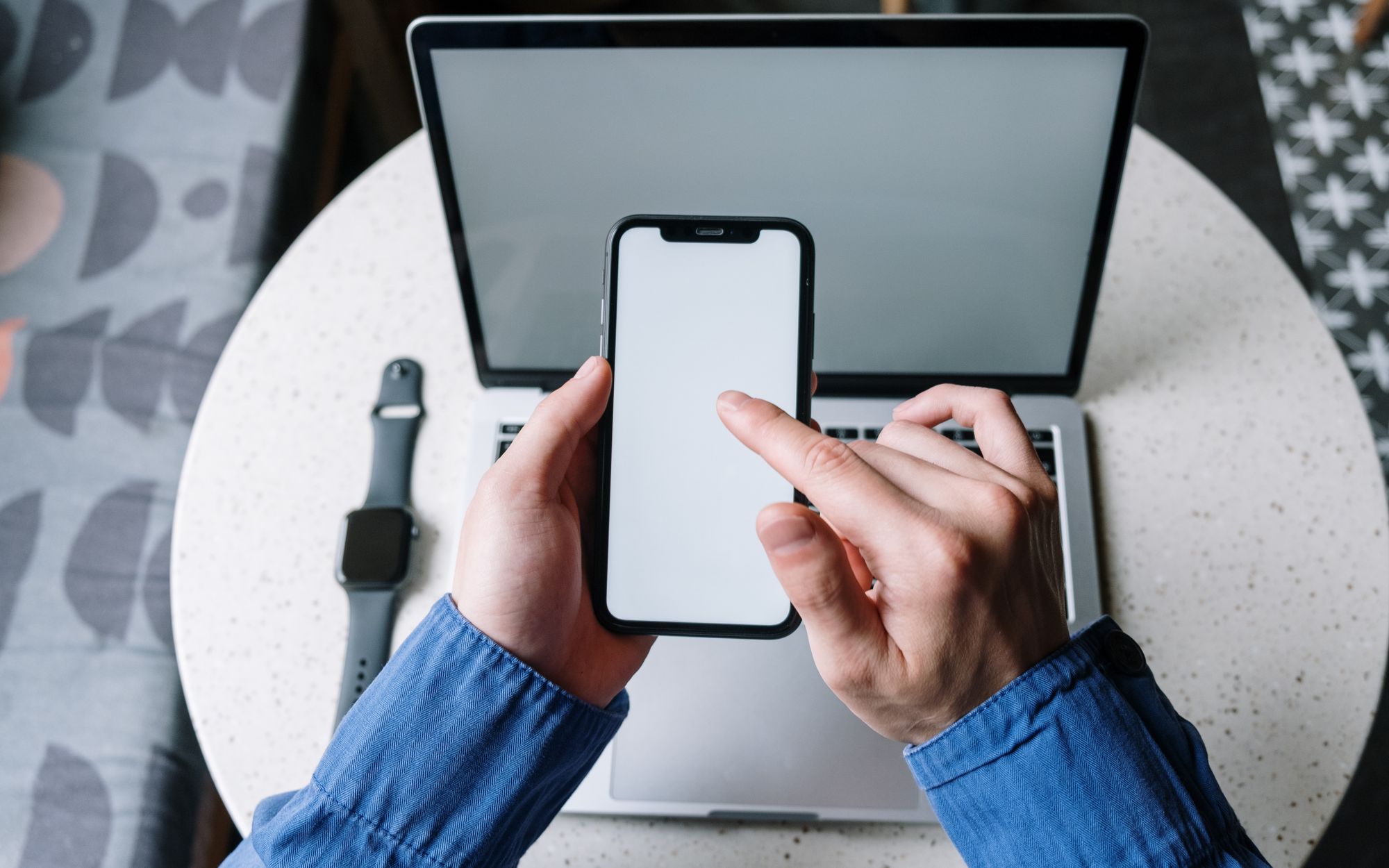 Person using a smartphone with a laptop and smartwatch nearby